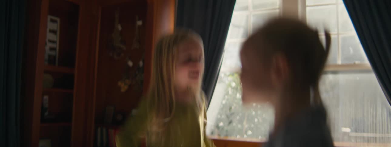 Children jumping on a bed in a room lit by natural light with wooden furniture and windows in the background