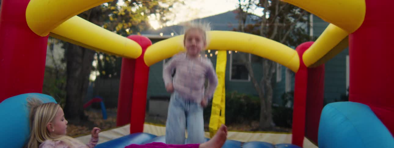 Little girl jumping in an inflatable bounce house as her sister is lying down relaxing