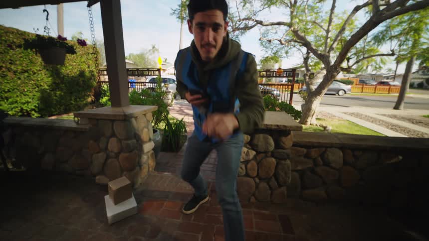 Delivery man leaves packages on the porch and takes a picture with his phone then rings the doorbell and waves as he leaves