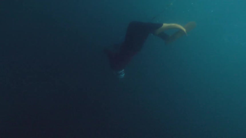 Person swims submerged in deep blue water with fins visible in motion