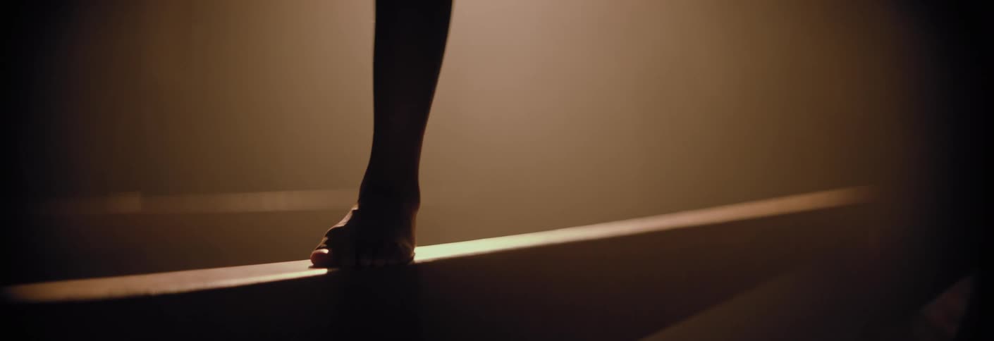A gymnast's bare feet seen performing a back walkover on a balance beam in dramatic lighting
