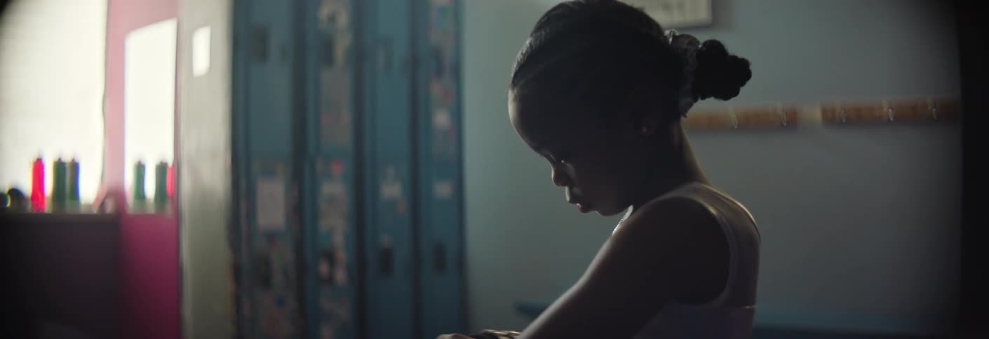 A young gymnast sits on a bench in a locker room carefully adjusting her white hand grips the scene is dimly lit highlighting her focused expression as she prepares for her routine