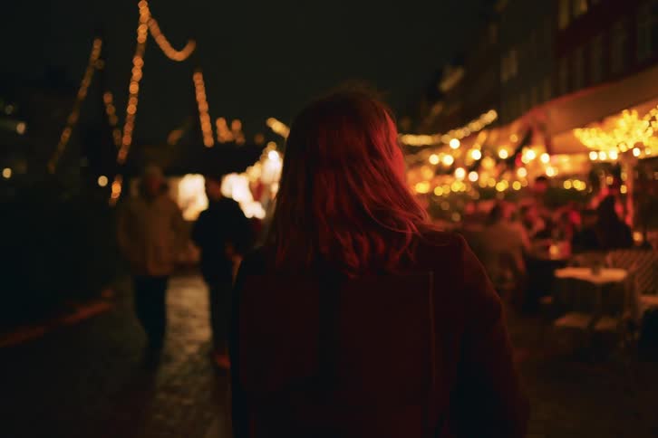 A woman walking along a city street at night with glowing lights all around