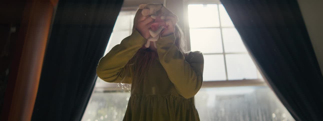 Blonde girl plays at home near the window as the sun shines in behind her