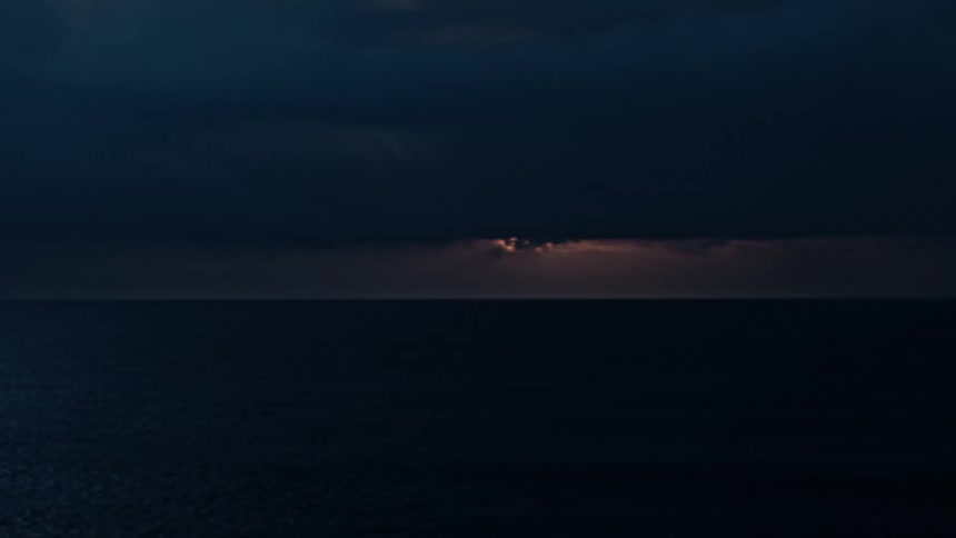 Moon beginning to break through in the overcast sky lightens the clouds over the water