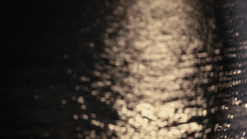 A dark calm body of water at night capturing the shimmering reflection of golden light on the surface