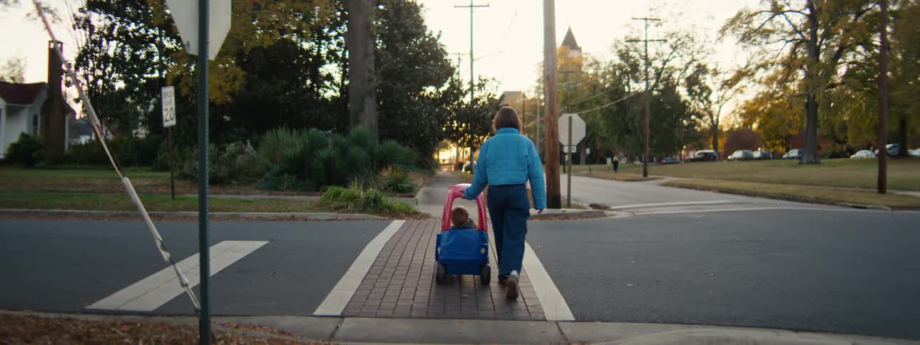A mother pushes her son in a wagon across a quiet suburban crosswalk at dusk during autumn