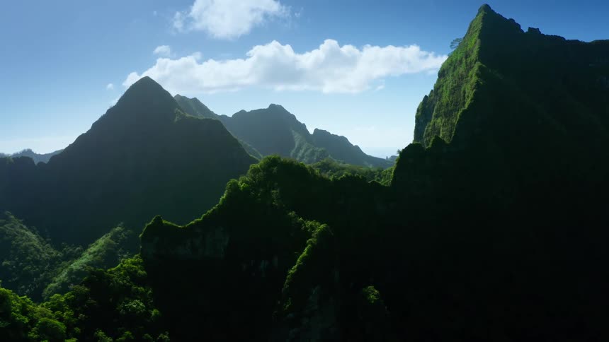 Aerial view of lush green mountains and deep valleys under clear blue sky