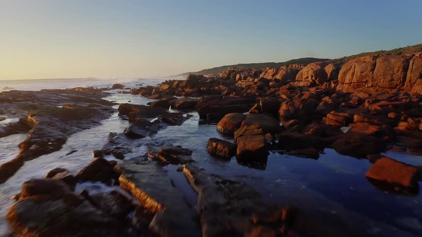 Waves roll in to shore and splash against rocks along the coast