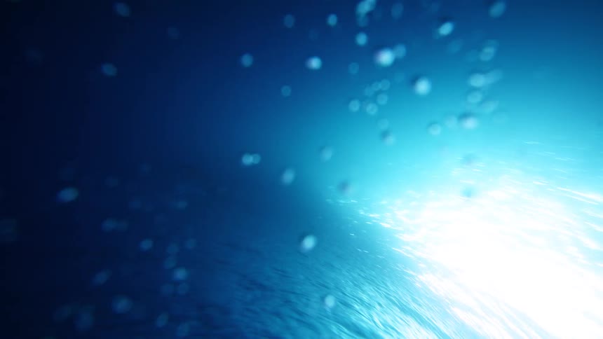 Water surface illuminated by a blue light beam with blurred particles in the foreground