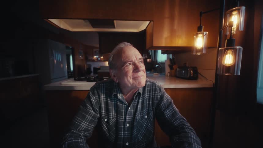Elderly man typing on a calculator in the dining room his expression happy