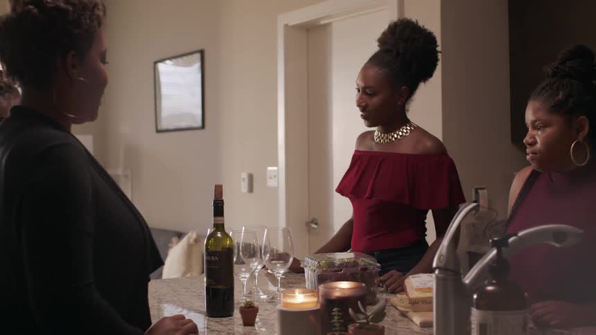 Women drink wine around a kitchen counter