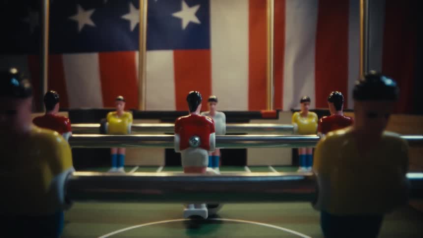 Player figures on a foosball table are lined up for a match in front of an american flag