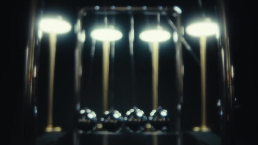 A newtons cradle shows polished metal spheres suspended beneath bright overhead lights creating a moody abstract sense of balance and motion