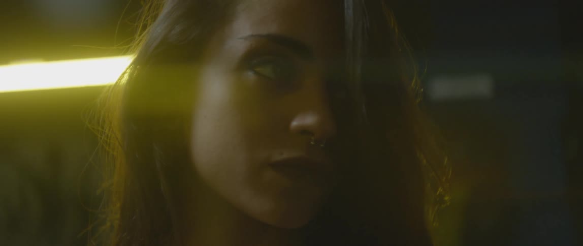 Close-up of a woman sitting in a dimly lit area before a fluorescent light