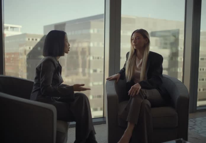 Two women sitting in chairs talking with a phone and notebook on the table