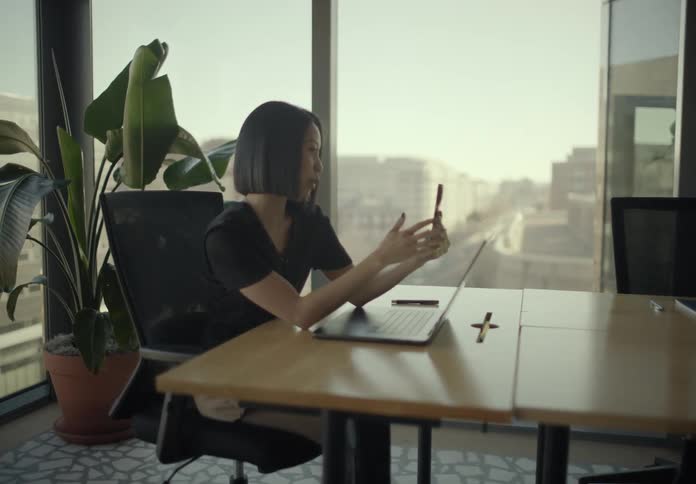 A smiling woman talks on her smartphone during a video call in a modern office