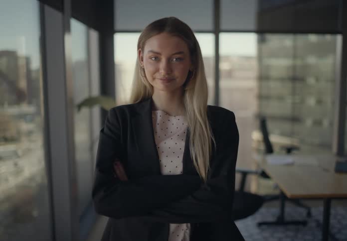 Woman standing with arms crossed in a modern office with table and glass windows in the background