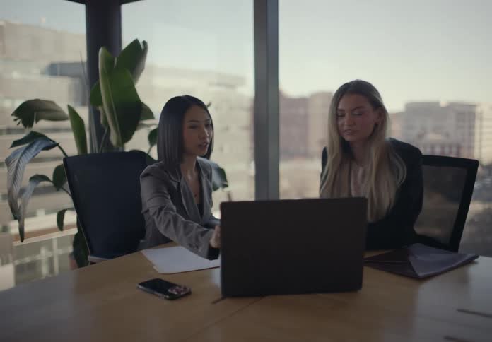 The coworkers talk at the desk while looking at a laptop