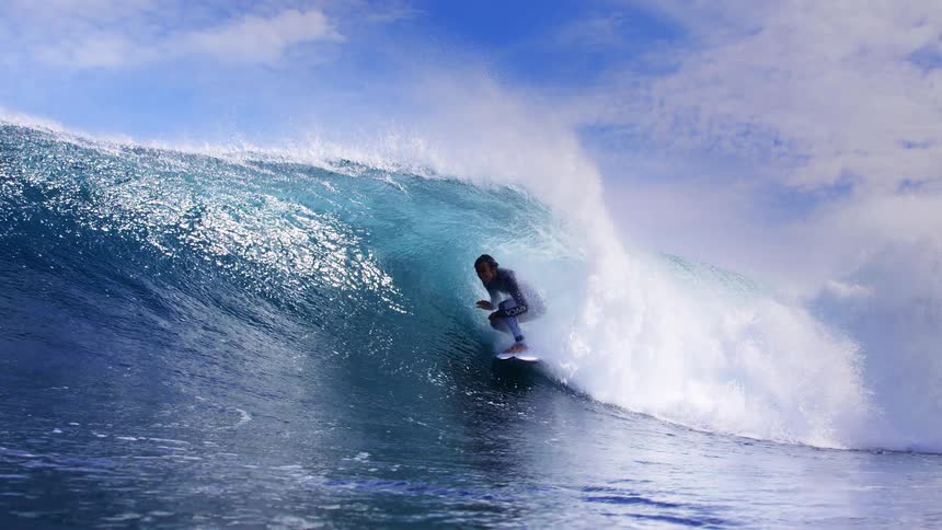 Surfer rides a big wave curling and splashing over him in the sunlight
