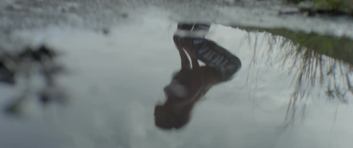A reflection of a woman stretching is visible in a puddle