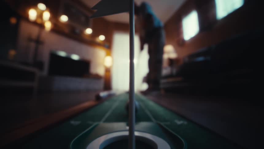 A soccer patterned golf ball rolls down an indoor putting green and drops into the hole