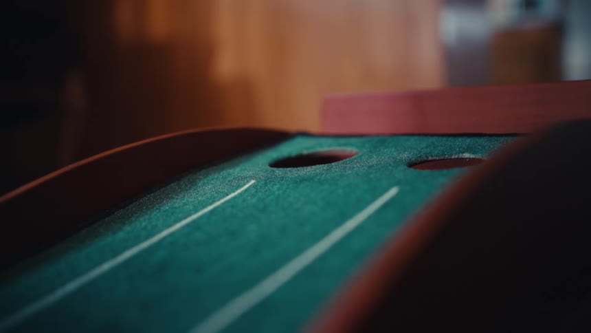 A golf ball rolls up a slanted wooden ramp covered in green felt toward circular targets in a game of indoor skeeball golf