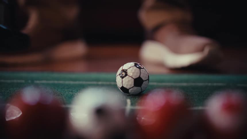 A person places a soccer patterned golf ball on an indoor putting mat and strikes it with a putter