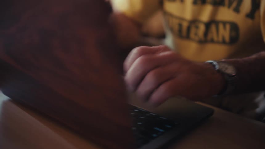 Man sitting at a table typing on a laptop computer keyboard
