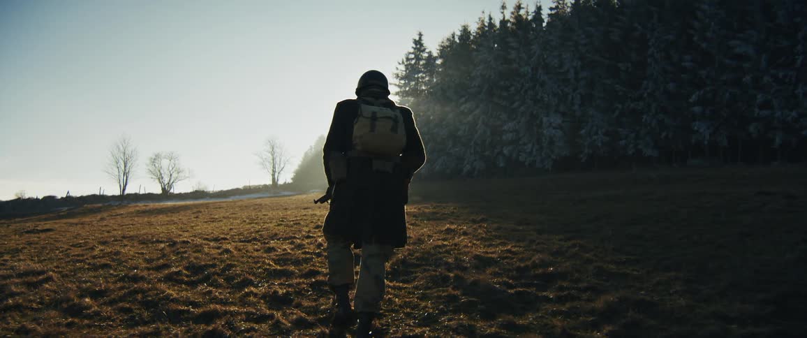 A military officer walking across a field at sunset wearing a uniform boots and a helmet