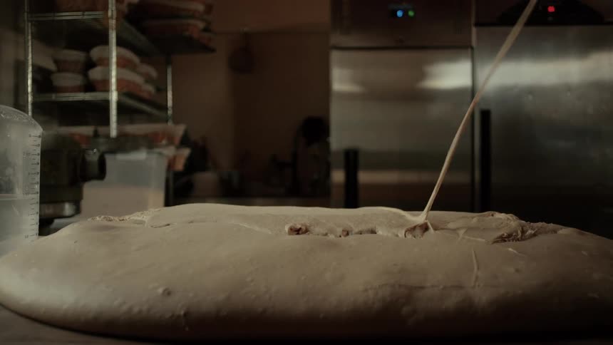 A chef pouring dough from a bowl onto a work surface inside a bakery