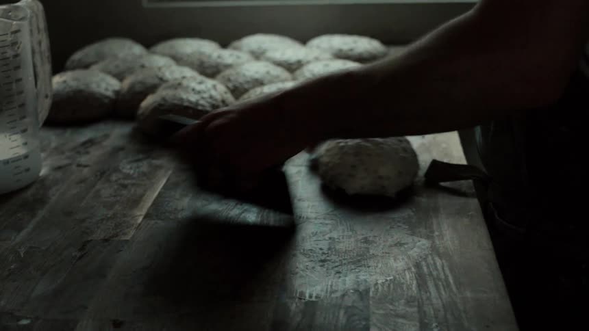 Portion of dough being handled on a wooden table with other dough portions in the background
