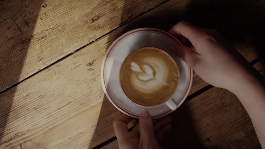 Pair of hands picking up a cappuccino cup