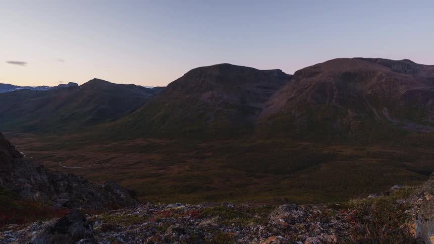 A mountain range in the wilderness during fall its slopes and valley floor covered in brown grasses glowing softly in the warm light of sunset