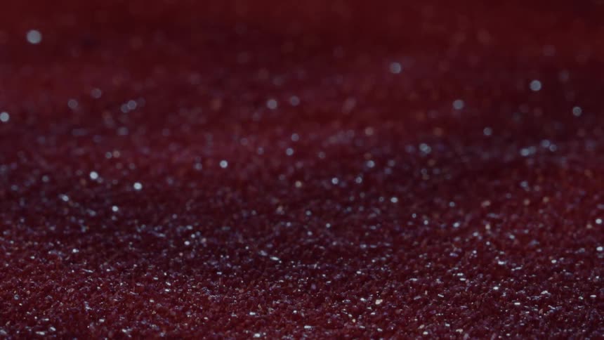 A rich deep red surface filled with countless tiny sparkling particles stretches across the frame creating a warm textured and almost velvety abstract scene with a subtle sense of depth and shimmer