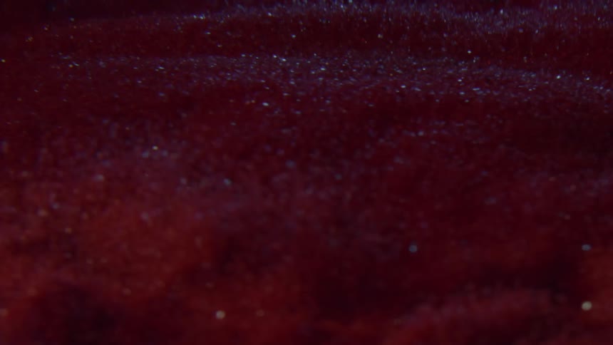 Reddish particles some reflective vibrate in a gray walled container