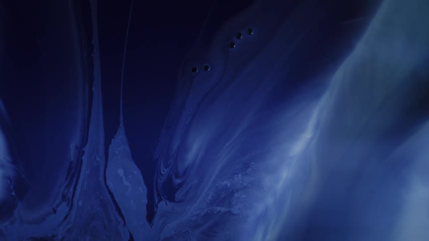Swirls of deep blue liquid diffuse slowly through a fluid medium creating ethereal shifting patterns that darken and fold over one another in a mesmerizing display