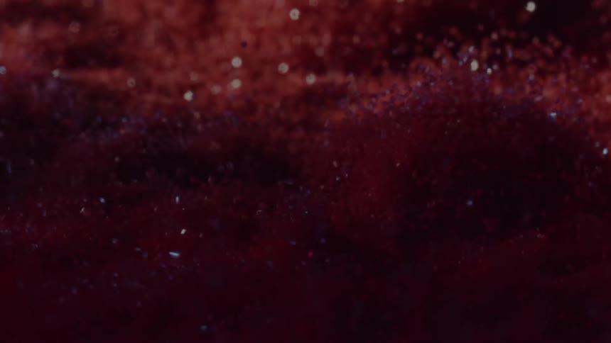 Deep red granular particles undulate in rhythmic waves catching the light to create a shimmering shifting landscape in this abstract closeup