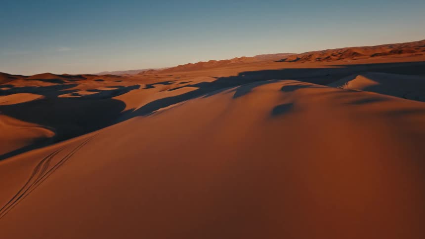 Sand dunes cast shadows as the sun shines on the desert