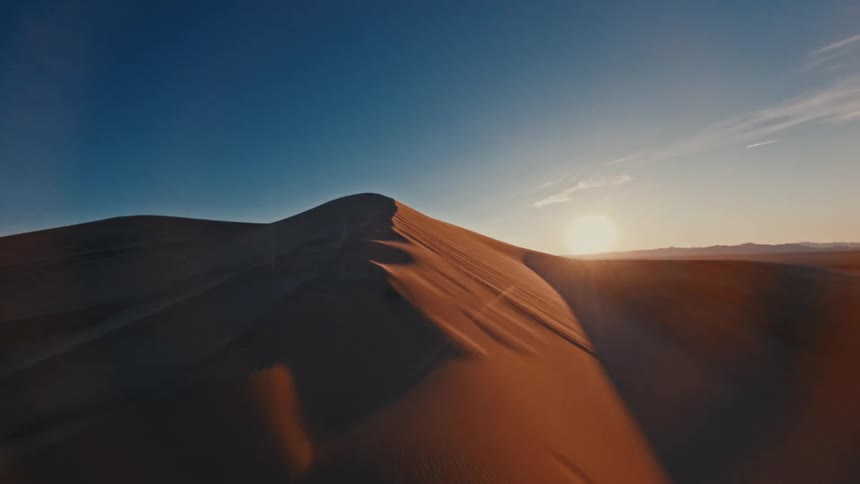 A lone sand dune rises against a twilight sky its peak catching the last golden light as the sun sets behind it