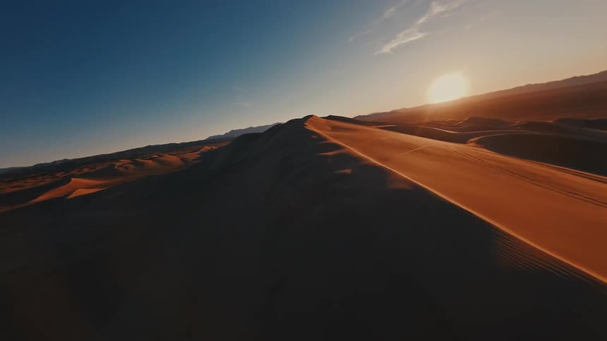 Sand dunes and erg across the desert as the sun shines on the horizon