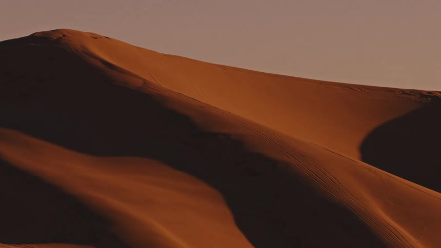 Sunlight shines upon the sloped surface of a large sand dune