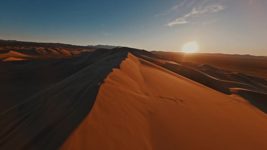 Tall sand dunes stretch across a quiet desert under a glowing sunset sky