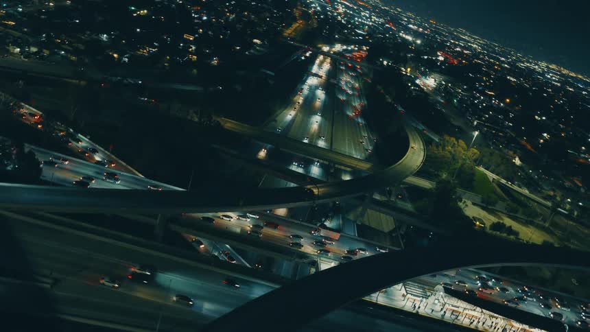 Aerial view of a sprawling city at night with a complex highway interchange and moving traffic