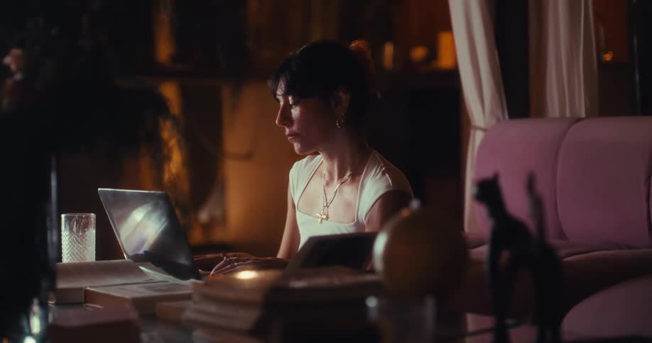 A woman typing on a laptop while seated indoor in a dark room