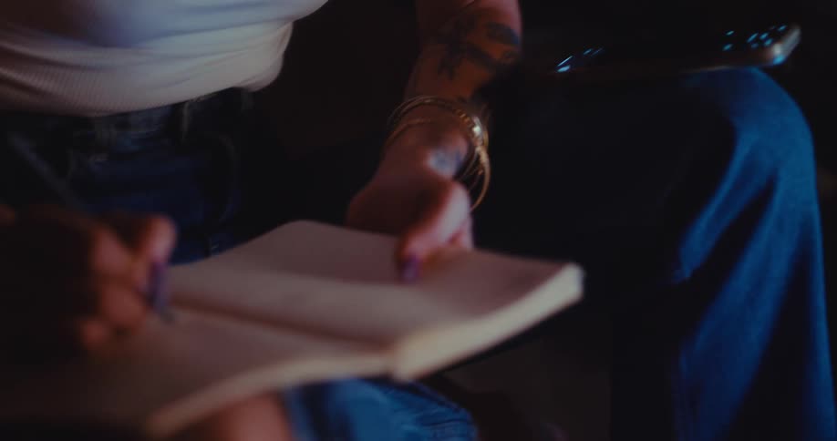 A person writing in a notebook while seated in a living room under soft low light