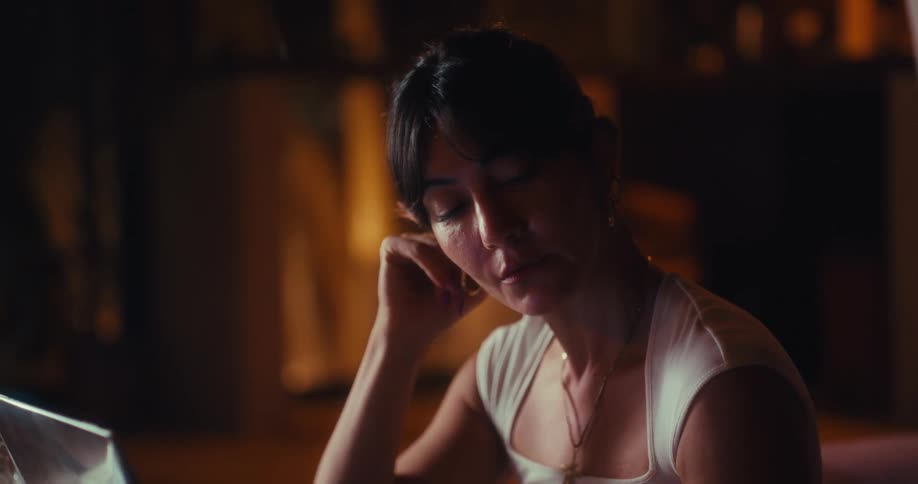 Woman sitting at a table thinking as she types on a laptop computer