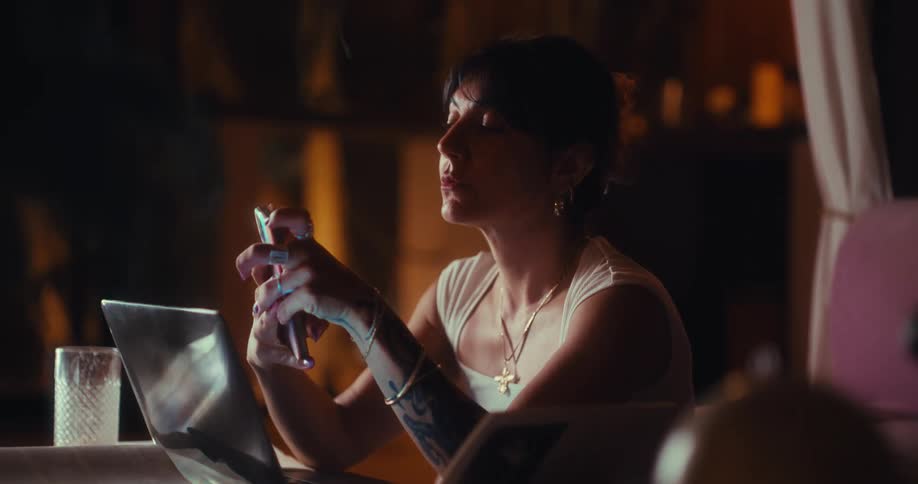Woman sitting interacting with her smartphone in front of a laptop