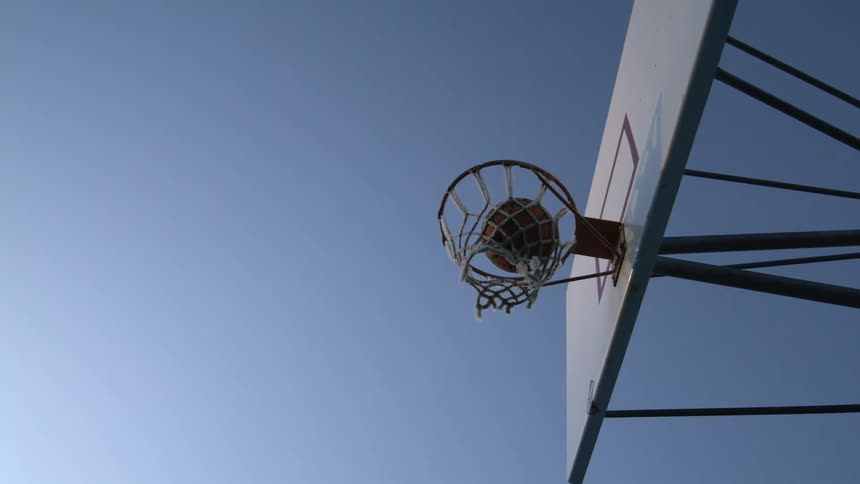 A basketball swishing through the hoop on an outdoor court under a clear blue sky