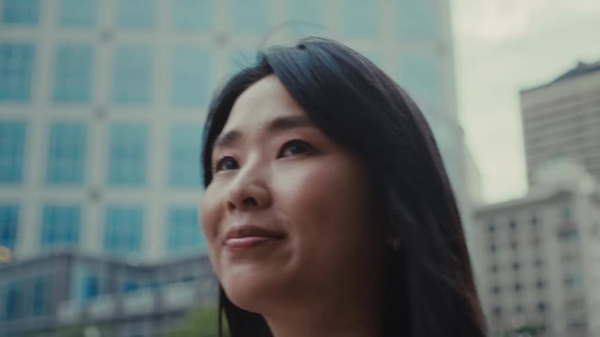 Female asian adult standing on the streets of a metropolitan area then smiling and walking away outdoors during day time